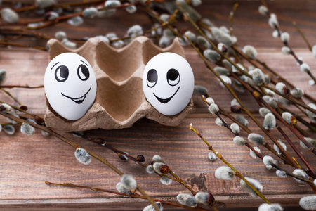 two white eggs with doodle cheerful faces and willow branches on wooden backgroundの写真素材