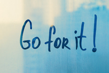Hand drawn message Go for it on foggy blue glass on city window
