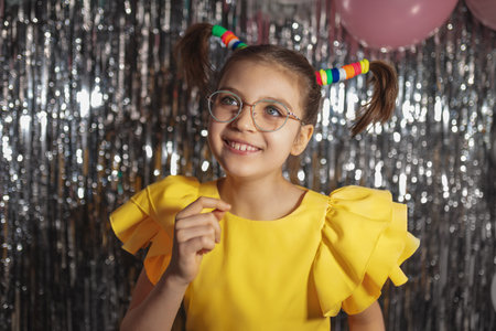 Happy funny girl in glasses and yellow holiday blouse with ponytails hairstyle on festive backgroundの写真素材
