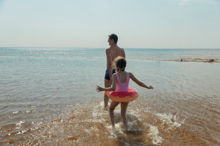 Father and daughter go swimming in sea on hot summer day view from backの写真素材