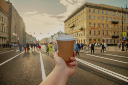 Brown paper cup of drink in womens hand on Nevsky Prospekt in center of St. Petersburg, Russiaの写真素材