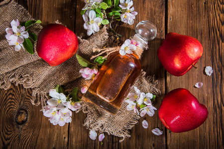 A bottle of apple cider vinegar (cider), fresh apples and apple-tree flowers on a wooden background. Country style.の写真素材