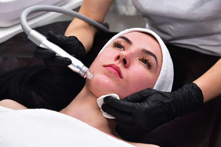 The beautician performs a facial cleansing procedure. Facial care, mask, scrub. Hardware facial cleansing. Skin rejuvenation and beauty.の写真素材