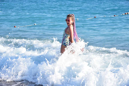 Cheerful little girl with colored pigtails on vacation on the background of the blue seaの写真素材