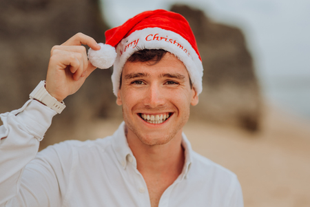 happy smiling and laughing handsome boy men in red hat Santa claus and white shirt stay on beach and hold credit card in oceanの写真素材