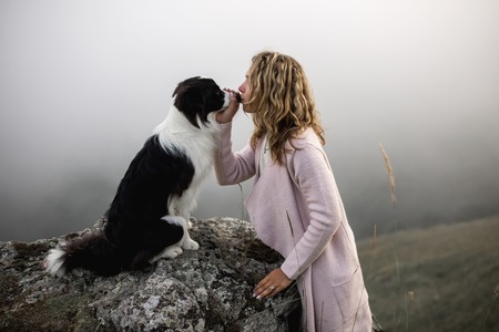 cool Girl kiss dog border collie on edge of rock in fogの写真素材