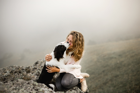 dog border collie lick cool girl on edge of rock in fogの写真素材