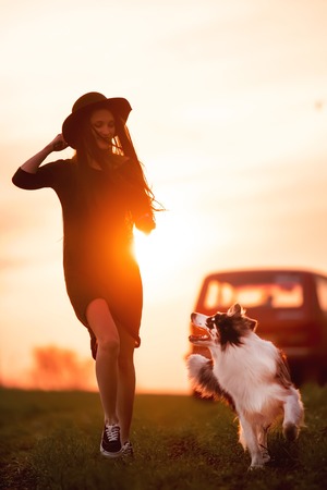 cool girl and dog border collie run on green field road in sunset togetherの写真素材
