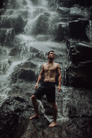 lean muscular Man look on waterfall in darkの写真素材