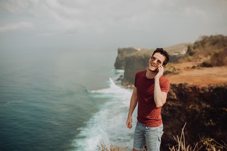 Young man using a cellphone on top a ocean cliffの写真素材