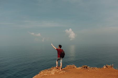 Young man using a backpack on top a ocean cliff, happy smiling emotionsの写真素材