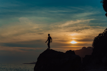Strong fitness yoga man on the rock beach near the ocean. Harmonic concept, peace and success. silhouetteの写真素材