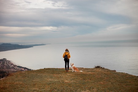 young beautiful woman enjoying the view with her dog during hiking trip in the mountain
