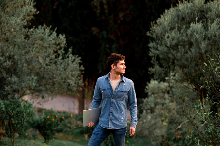 Man in jeans suit standing with a laptop in garden with mandarins
