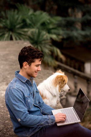happy smiling Man in jeans suit with red dog border collie sit with a laptop in gardenの写真素材