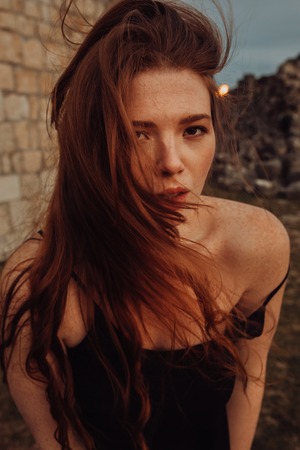 Portrait Trendy girl with hairstyle with red lips in black print dress on summer garden. mandarins. Redhead model in trendy summer dress in garden. Stylish hairstyleの写真素材