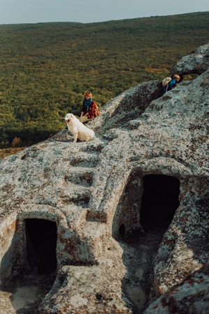beautiful women and white dog sit on a stone in the stone castle. in the background mountains