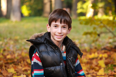 Boy in sunny autumn park sitting on leavesの写真素材