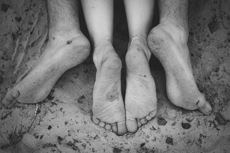 Feet of two persons guy girl lie on dirty beach, men and women heels and toes in sand, top viewの写真素材