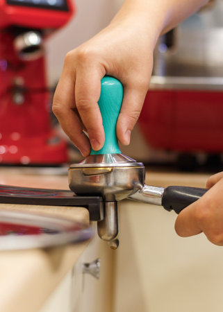 Hands barista tamper to grind coffee beans  puck pressing in coffee shop. inside, close-up, side view, verticalの写真素材