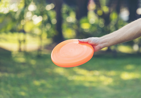 Hand man throwing orange frisbee disk in the parkの写真素材