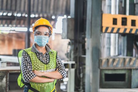 Asian female engineers wearing hygienic mask protect with helmet safety in factory. Coronavirus...