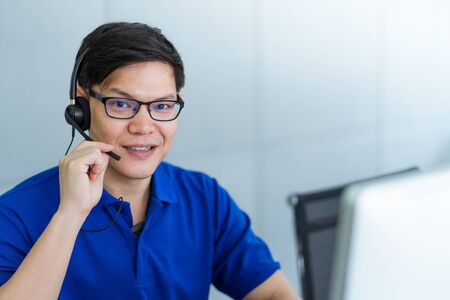 Call center man in blue shirt uniform working care customer service wearing headphone talking with customer at call center office.Support Customer Team 24 hoursの写真素材