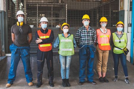 Group of diverse team of workers wearing face mask and protective helmets standing in front of the factoryの写真素材
