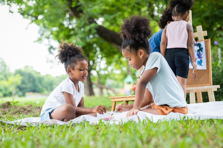 African American little girls with curly hair painting watercolor in summer park. Kid artist painter draw pictures outside.Education learning outdoor conceptの写真素材