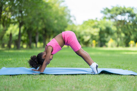 African American little girl practicing yoga on roll mat in the park. Kids afro girl with curly hair engaged in training yoga outdoor.の写真素材