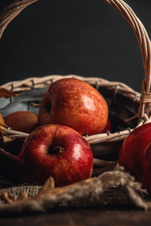 Autumn composition with fresh red apples in a wooden basket on rustic wooden background. Red apples on linen backgroundの写真素材