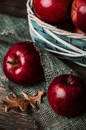 Autumn composition with fresh red apples in a wooden basket on rustic wooden background. Red apples on linen backgroundの写真素材
