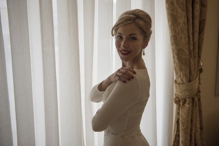 Young beautiful bride standing at the windowの写真素材