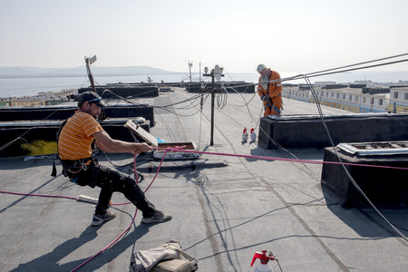 Steeplejack (house painter) checks his equipment on the roof of the buildingの写真素材