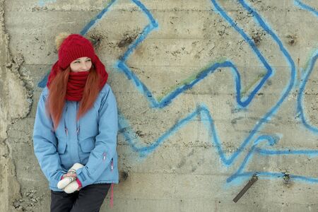 Portrait of young beautiful woman in red hat and red comforter standing against grunge concrete wallの写真素材