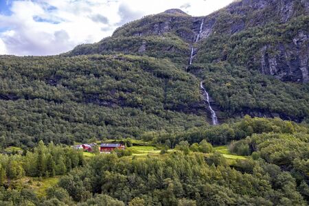 Norwegian farm at the foot of the mountain against the waterfallの写真素材