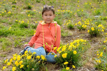Little chukchi girl sitting among the flowering dandellionsの写真素材