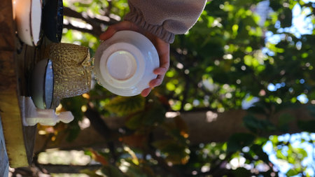 A gentle hand pours fragrant tea into a delicate cup in a serene outdoor setting surrounded by lush greeneryの写真素材