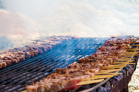 Chicken and lamb skewers on a simple, rustic grill laid out on the sand of a greek island. Close up of smocking meat being cooked.の写真素材