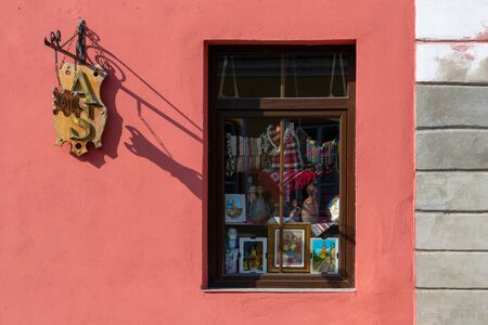 Sibiu, Romania - March 25, 2019: Souvenir shop with traditional Romanian clothing and paintings of Sibiu (Hermannstadt). Minimalist street shop window on a light red wall and a carved wooden sign.のeditorial素材