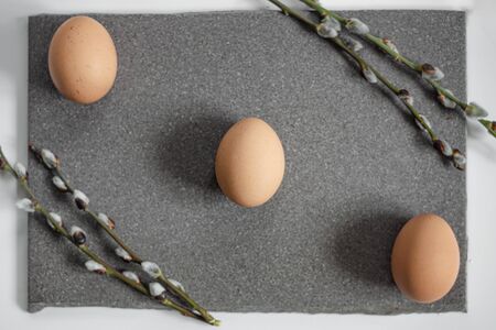 Three beige eggs lie on the granite surface, willow twigs in the corners.の写真素材