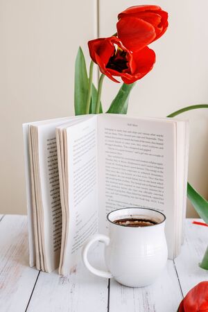 beautiful mug with hot coffee, reading a book in the morning, spring red tulipの写真素材