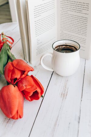 beautiful mug with hot coffee, reading a book in the morning, spring red tulipの写真素材