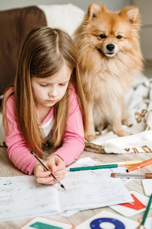 Cute girl studying at home and drawing on wooden warm floorの写真素材