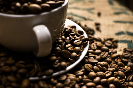 Close up of a white coffee cup full of coffee beans, surrounded by even more coffee beansの写真素材