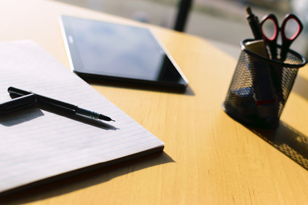 pen, paper and tablet on table at big wiindow. Shadows falling from pen cannisterの写真素材