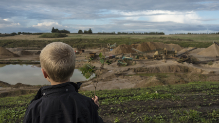 Innocent Young boy standing in front of a quarry in a green landscape. Witnessing the destruction mankind have made in nature. What have we done to natureの写真素材