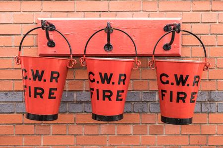 Three red C.W.R water bucket hanging against a brick wallの写真素材