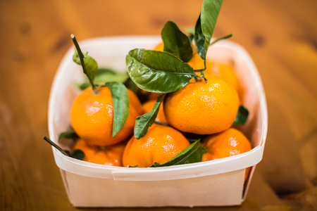 A bowl of mandarin oranges with green stalks and leaves.の写真素材
