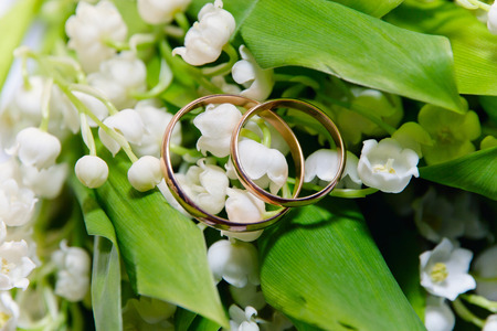 Two gold wedding rings against the background of lilies of the valleyの写真素材